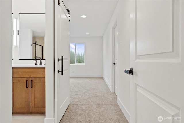 corridor featuring recessed lighting, light colored carpet, a sink, and baseboards