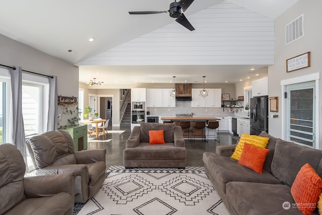 living room with ceiling fan with notable chandelier and high vaulted ceiling