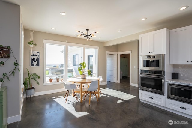 kitchen with decorative backsplash, light stone counters, white cabinets, a chandelier, and stainless steel microwave