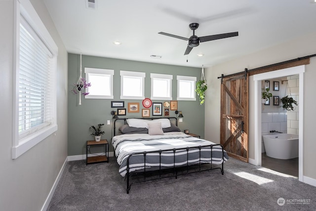 bedroom with ensuite bathroom, dark carpet, ceiling fan, a barn door, and multiple windows