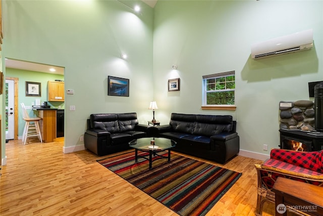 living room featuring an AC wall unit, a high ceiling, light wood finished floors, and a wood stove