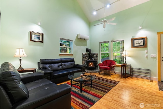 living room with high vaulted ceiling, track lighting, wood finished floors, a wall unit AC, and a wood stove