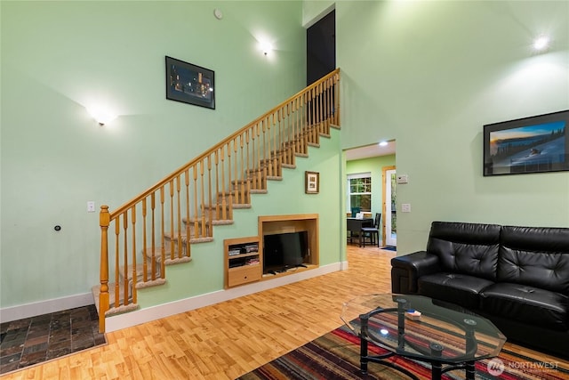 living area featuring a towering ceiling, baseboards, wood finished floors, and stairs