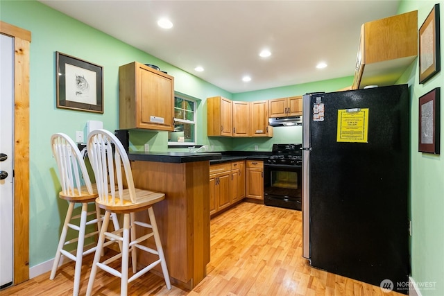 kitchen with under cabinet range hood, a kitchen breakfast bar, freestanding refrigerator, black gas range oven, and a peninsula