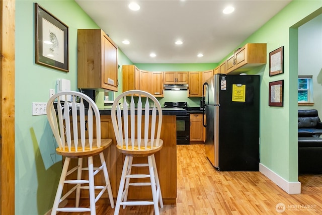 kitchen featuring a peninsula, freestanding refrigerator, black range with electric stovetop, under cabinet range hood, and dark countertops