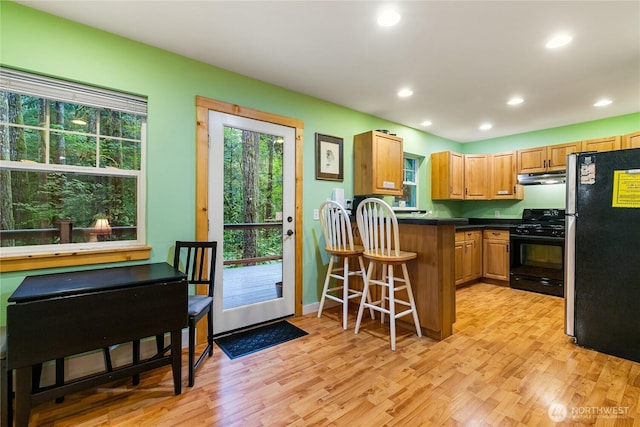 kitchen featuring black gas stove, freestanding refrigerator, light wood-style floors, under cabinet range hood, and dark countertops