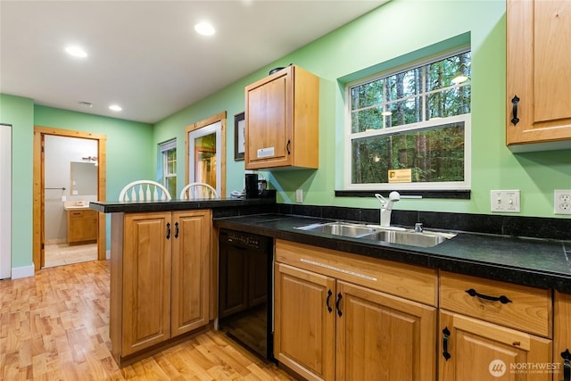 kitchen featuring a sink, black dishwasher, dark countertops, and light wood-style flooring