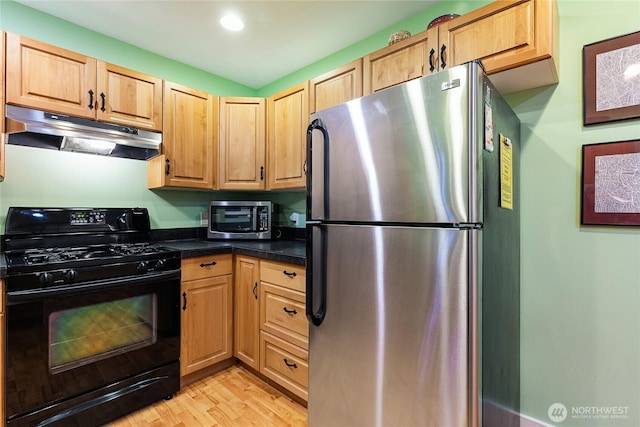 kitchen with light brown cabinetry, stainless steel appliances, under cabinet range hood, dark countertops, and light wood-type flooring