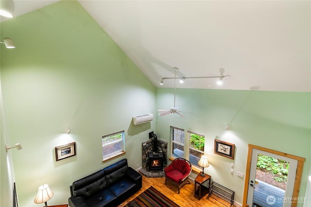 living area featuring high vaulted ceiling, track lighting, a wall mounted AC, wood finished floors, and a wood stove