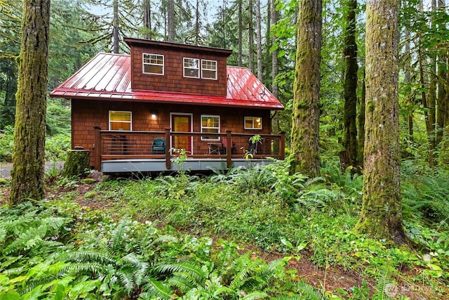 view of front of home featuring covered porch, a wooded view, metal roof, and a standing seam roof