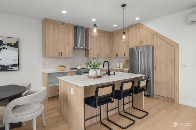 kitchen featuring hanging light fixtures, premium appliances, light stone countertops, an island with sink, and wall chimney exhaust hood