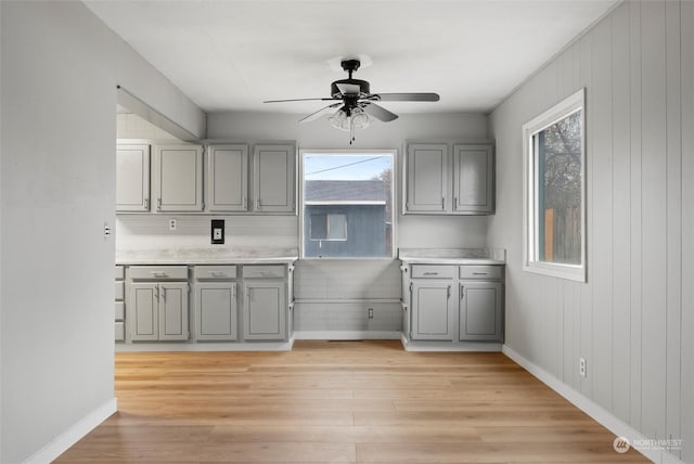 kitchen featuring gray cabinetry, ceiling fan, wooden walls, and light hardwood / wood-style floors