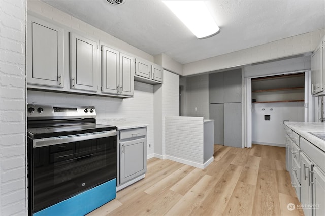 kitchen featuring a textured ceiling, gray cabinets, light hardwood / wood-style flooring, and stainless steel electric range