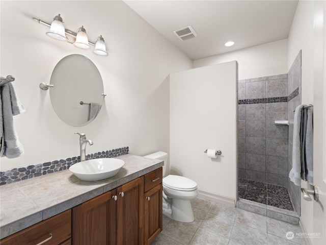 bathroom with tile patterned flooring, vanity, toilet, and a tile shower