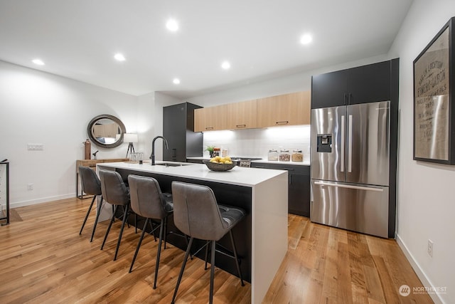 kitchen featuring stainless steel fridge, light brown cabinetry, light hardwood / wood-style flooring, a breakfast bar area, and an island with sink