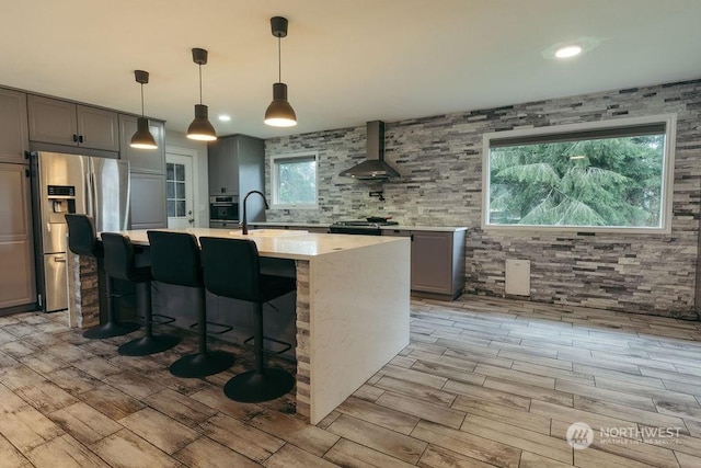 bar featuring stainless steel appliances, gray cabinets, hanging light fixtures, and wall chimney range hood