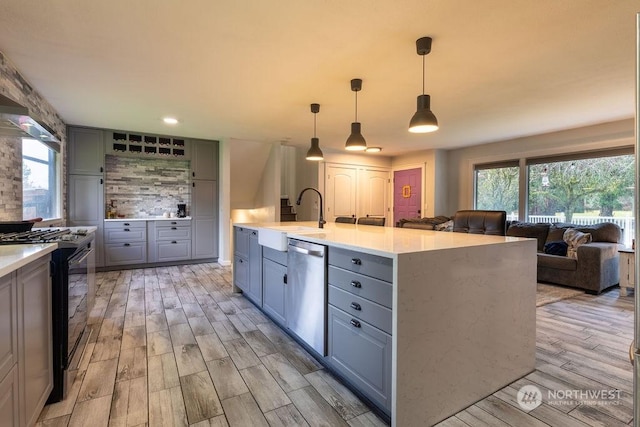 kitchen featuring gas range, dishwasher, sink, decorative light fixtures, and a center island with sink