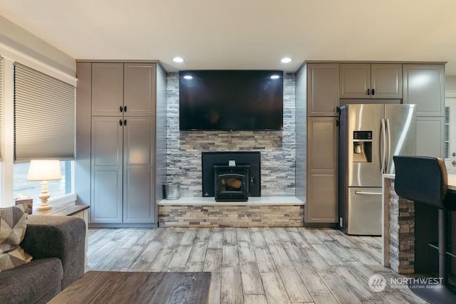 kitchen featuring light hardwood / wood-style floors, gray cabinets, stainless steel fridge with ice dispenser, and a wood stove