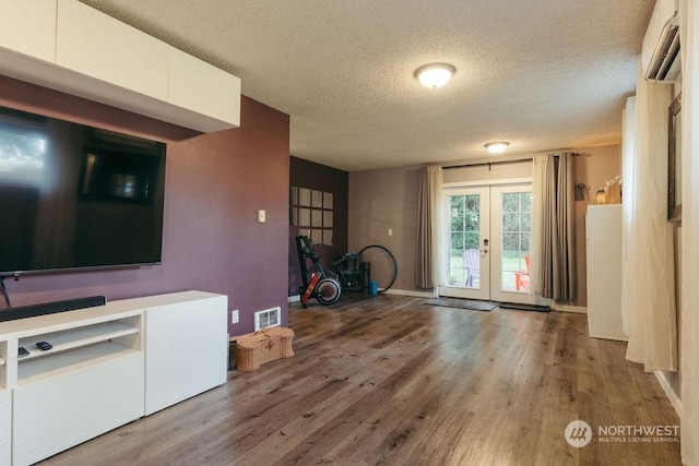 unfurnished living room featuring french doors, a textured ceiling, an AC wall unit, and hardwood / wood-style floors