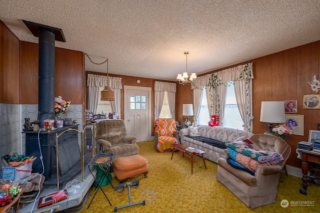 living room featuring a textured ceiling, wooden walls, an inviting chandelier, carpet floors, and a wood stove