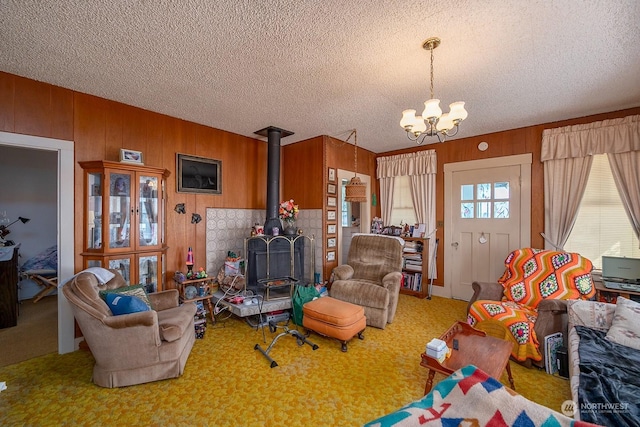 carpeted living room featuring a notable chandelier, a wood stove, a textured ceiling, and wooden walls