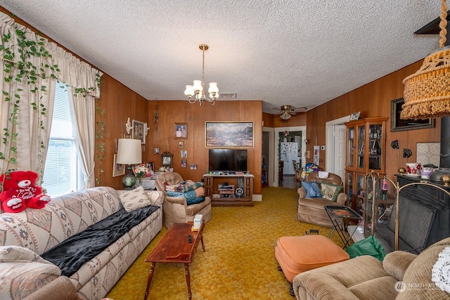 carpeted living room featuring ceiling fan with notable chandelier, a textured ceiling, and wooden walls