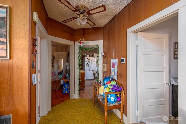 hall featuring carpet flooring, wood walls, and a textured ceiling