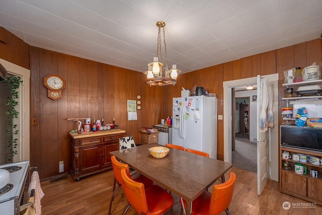 dining area featuring light wood-type flooring, wooden walls, and a notable chandelier