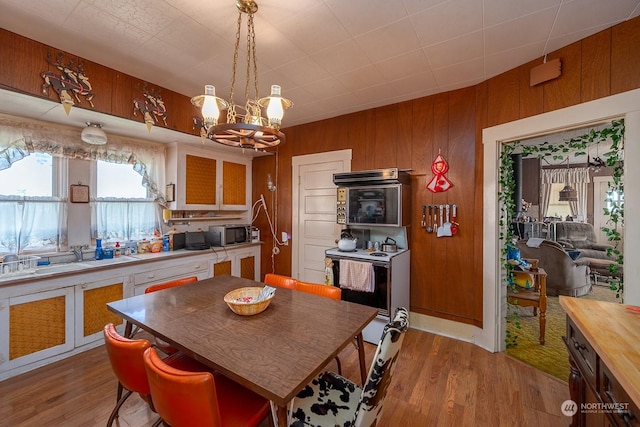 kitchen with sink, wood walls, a chandelier, decorative light fixtures, and light hardwood / wood-style floors