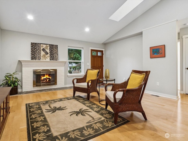 sitting room with lofted ceiling with skylight, a fireplace, and light hardwood / wood-style floors