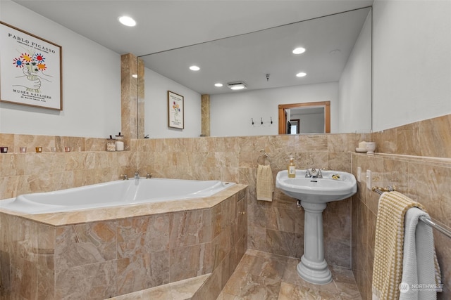 bathroom featuring a relaxing tiled tub and tile walls