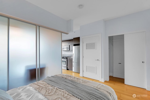 bedroom featuring stainless steel fridge and light hardwood / wood-style flooring