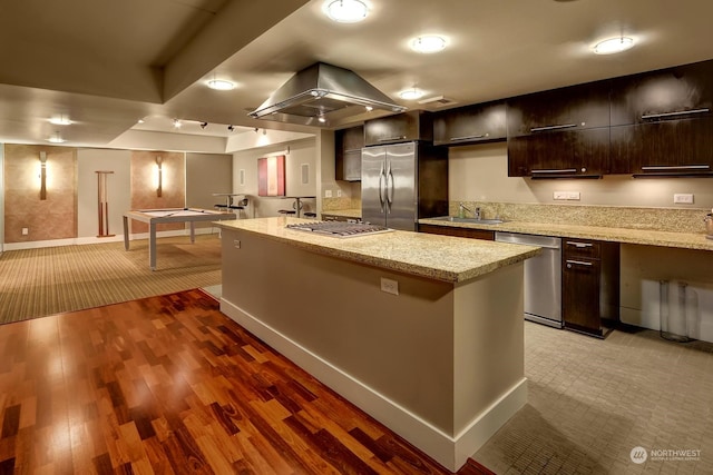 kitchen featuring a center island, light stone countertops, appliances with stainless steel finishes, island range hood, and dark brown cabinetry