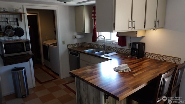 kitchen featuring wood counters, dishwasher, sink, separate washer and dryer, and white cabinetry