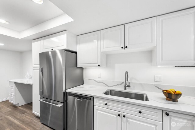 kitchen with white cabinetry, sink, stainless steel appliances, hardwood / wood-style floors, and a tray ceiling