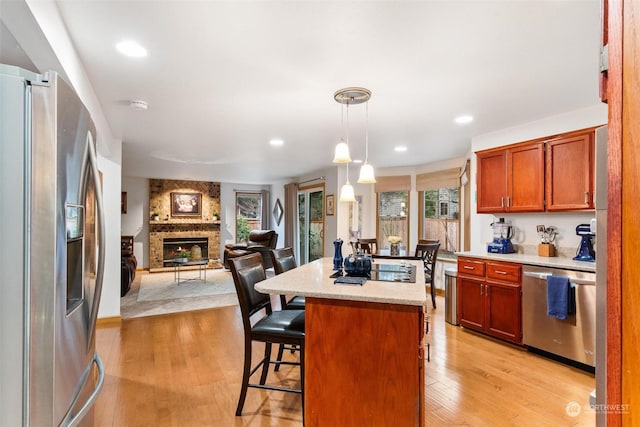 kitchen featuring appliances with stainless steel finishes, a large fireplace, pendant lighting, a kitchen island, and a breakfast bar area