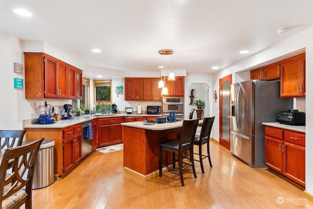 kitchen with a center island, light hardwood / wood-style flooring, decorative light fixtures, a kitchen bar, and appliances with stainless steel finishes