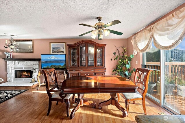 dining area featuring a textured ceiling, a fireplace, ceiling fan with notable chandelier, and hardwood / wood-style flooring