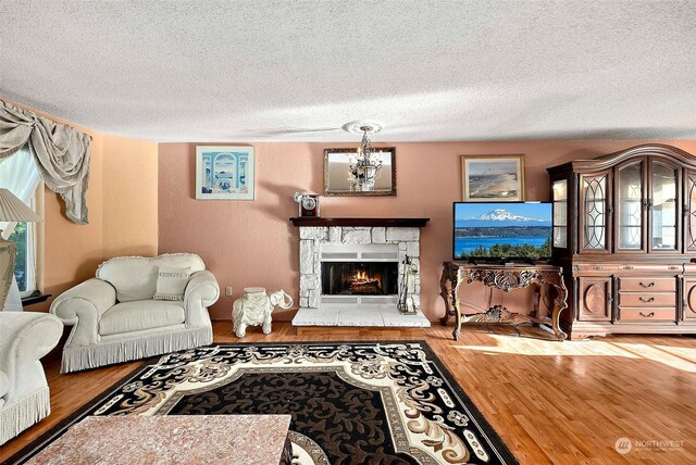 living room with wood-type flooring, a textured ceiling, a stone fireplace, and a notable chandelier