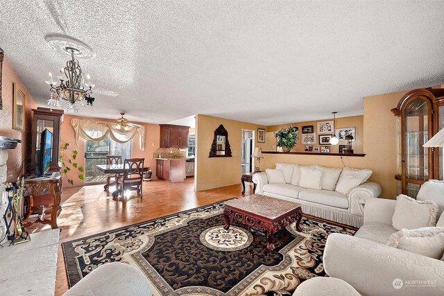 living room with ceiling fan with notable chandelier, a textured ceiling, and light hardwood / wood-style flooring