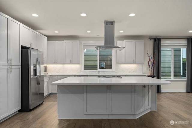 kitchen with stainless steel fridge, island range hood, hardwood / wood-style flooring, a center island, and white cabinetry