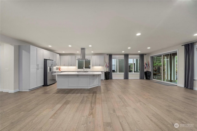 kitchen with light wood-type flooring, island range hood, stainless steel fridge with ice dispenser, a center island, and white cabinetry