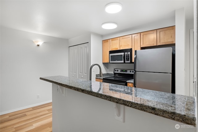 kitchen featuring a kitchen breakfast bar, kitchen peninsula, appliances with stainless steel finishes, and dark stone counters