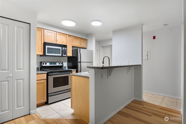 kitchen featuring light brown cabinets, sink, a breakfast bar area, light tile patterned floors, and stainless steel appliances