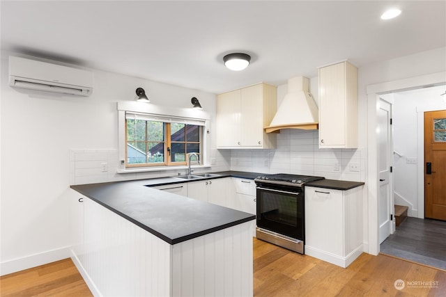 kitchen with kitchen peninsula, a wall mounted air conditioner, premium range hood, stainless steel range, and sink