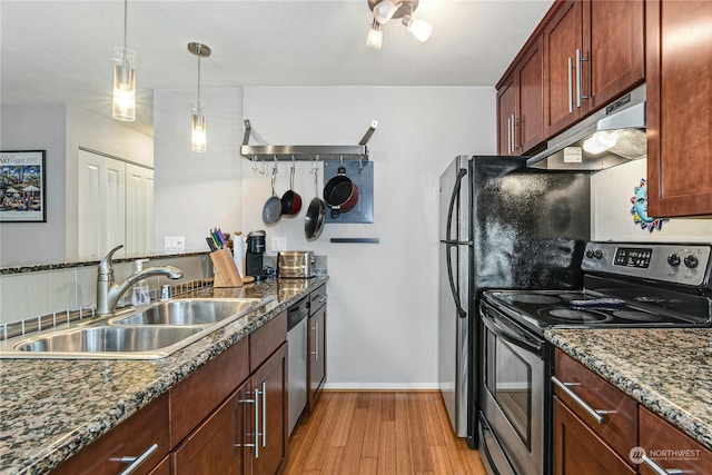 kitchen featuring dark stone countertops, light hardwood / wood-style floors, stainless steel appliances, sink, and decorative light fixtures