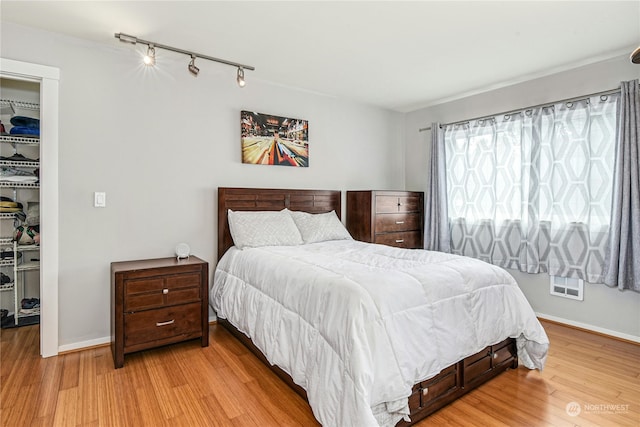 bedroom with light wood-type flooring, rail lighting, and a closet