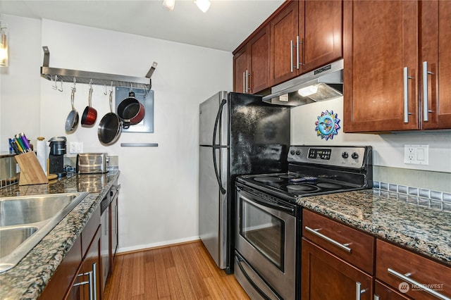 kitchen featuring light wood-type flooring, appliances with stainless steel finishes, dark stone countertops, and sink