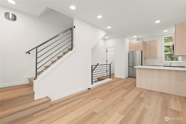 kitchen featuring sink, light hardwood / wood-style flooring, stainless steel fridge, light brown cabinetry, and tasteful backsplash