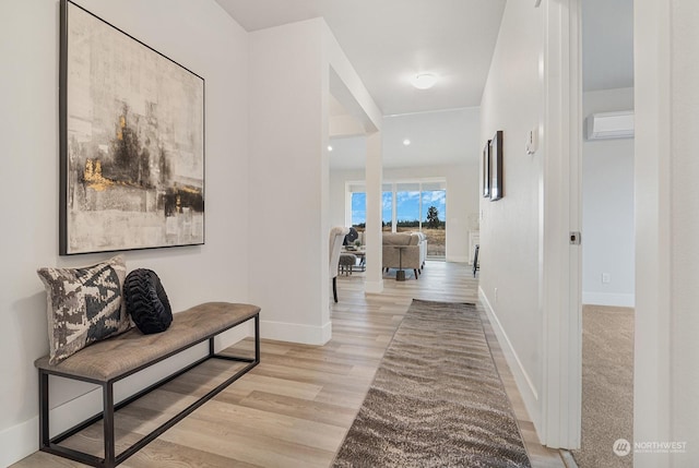 hallway with a wall mounted air conditioner and light hardwood / wood-style flooring